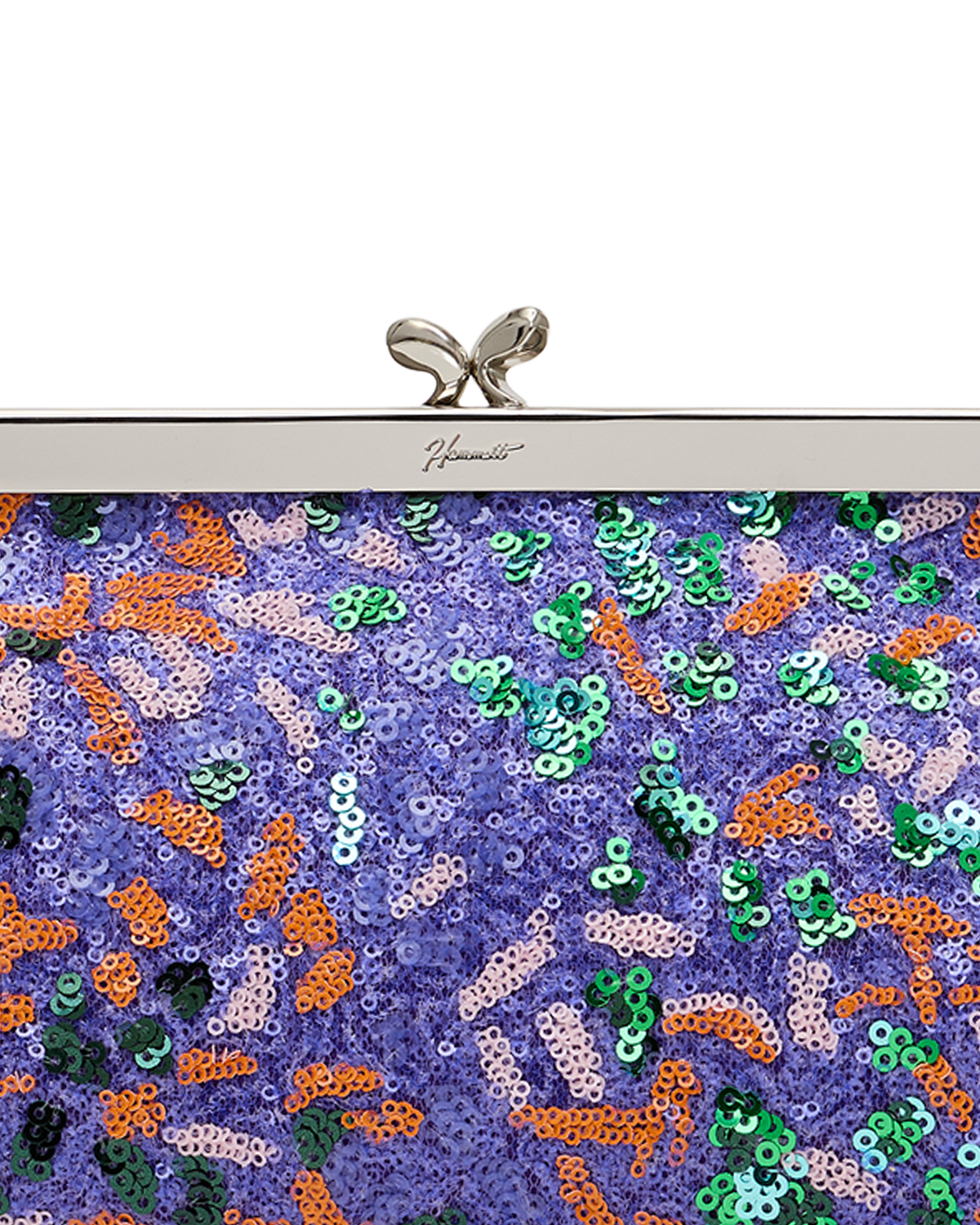 Close-up of a sequined clutch bag with a purple base covered in multicolored sequins in green, orange, and pink, featuring a silver metal top bar and bow clasp.