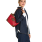 A woman in a denim outfit carries a red leather tote bag with brown trim and a circular logo patch on a plain white background.