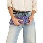 A person wearing a cream blouse, black belt, and light-wash wide-leg jeans holds a purple floral clutch bag against their hip against a plain white background.