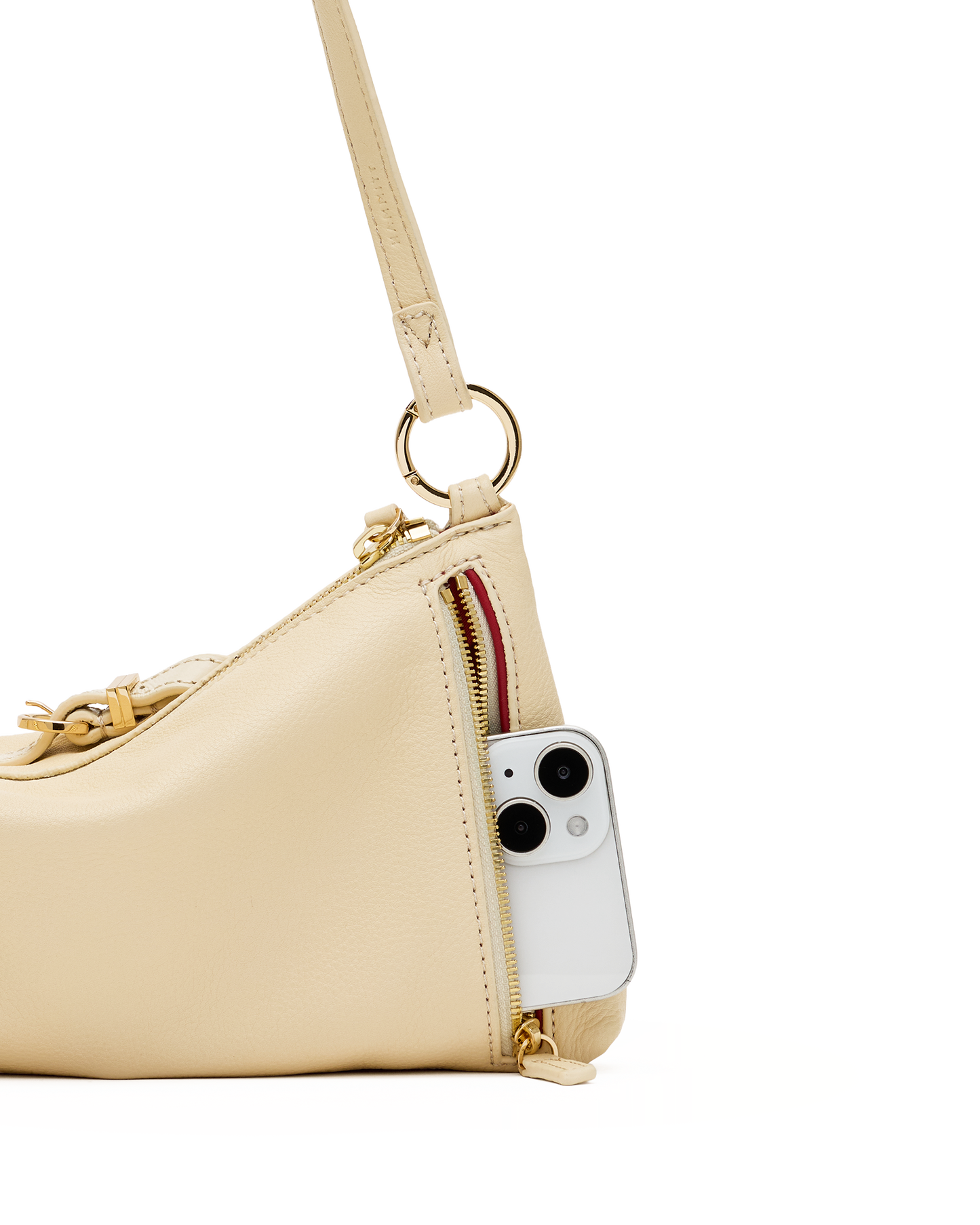A close-up of a light beige leather shoulder bag with gold-tone hardware, featuring a side zipper pocket containing a white smartphone, set against a plain white background.