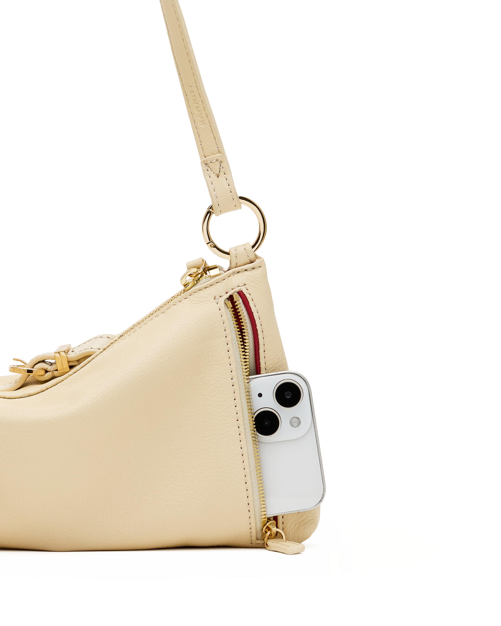 A close-up of a light beige leather shoulder bag with gold-tone hardware, featuring a side zipper pocket containing a white smartphone, set against a plain white background.