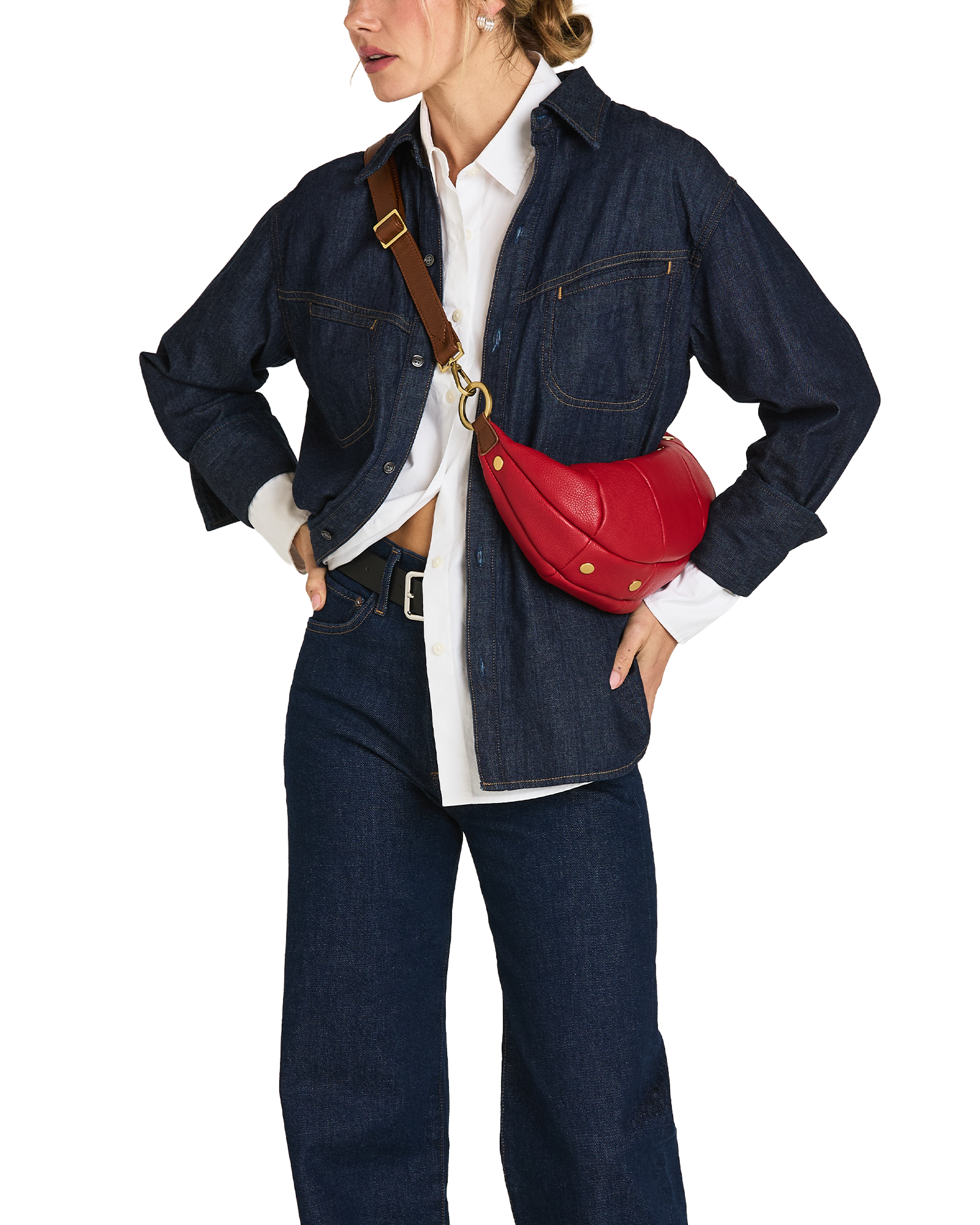 A model wearing a dark indigo denim jacket and matching wide-leg jeans, styled with a white button-down shirt, a black belt, and a bright red leather crescent-shaped crossbody bag with a brown strap and gold hardware.