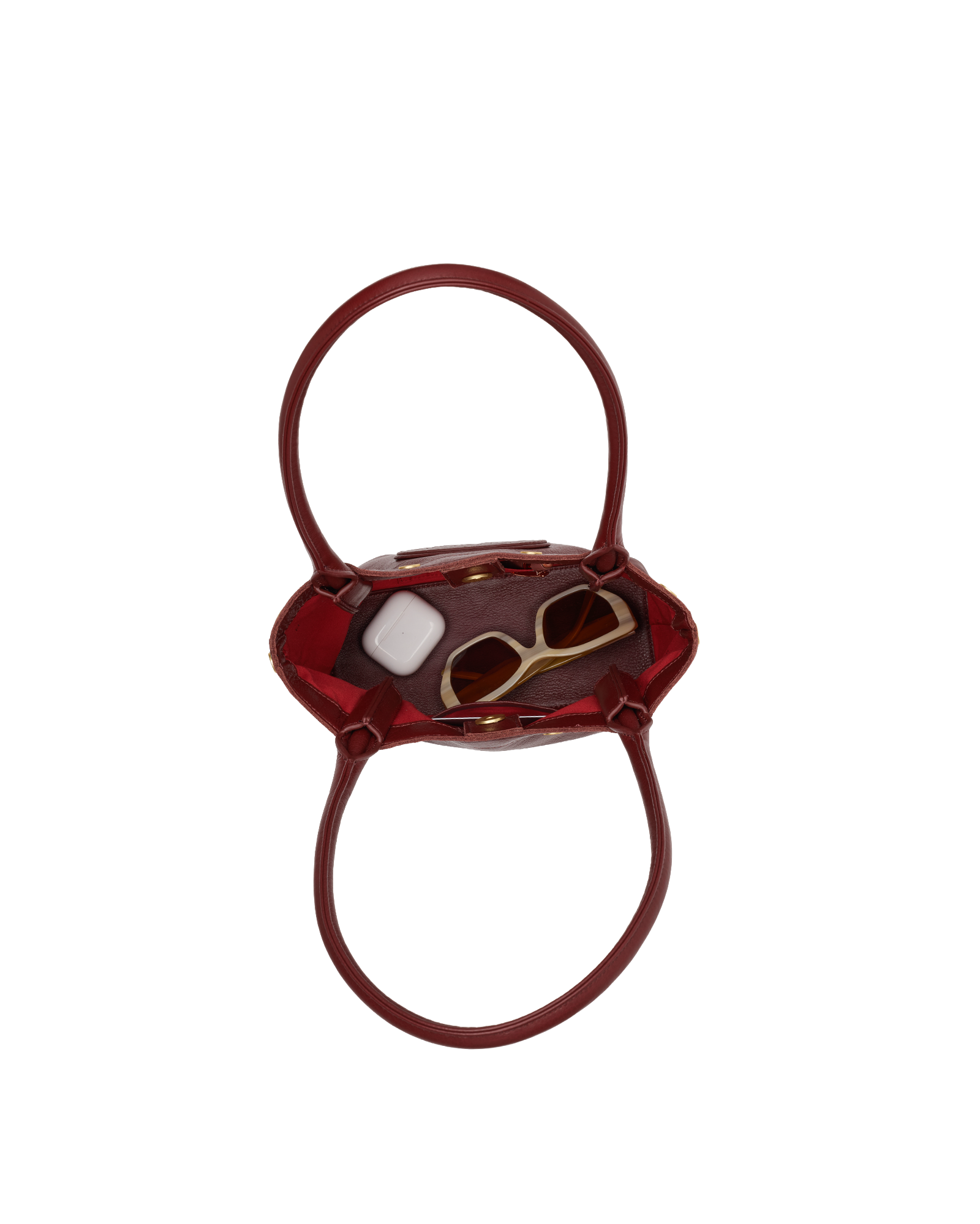 A small glossy burgundy handbag with a top handle, shown from above on a plain white background. Inside the bag, a pair of gold-framed sunglasses and a white rectangular item are partially visible.