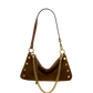 A brown suede crescent-shaped shoulder bag with gold-tone hardware, featuring a long shoulder strap, a gold chain link detail, and decorative gold studs on the sides.