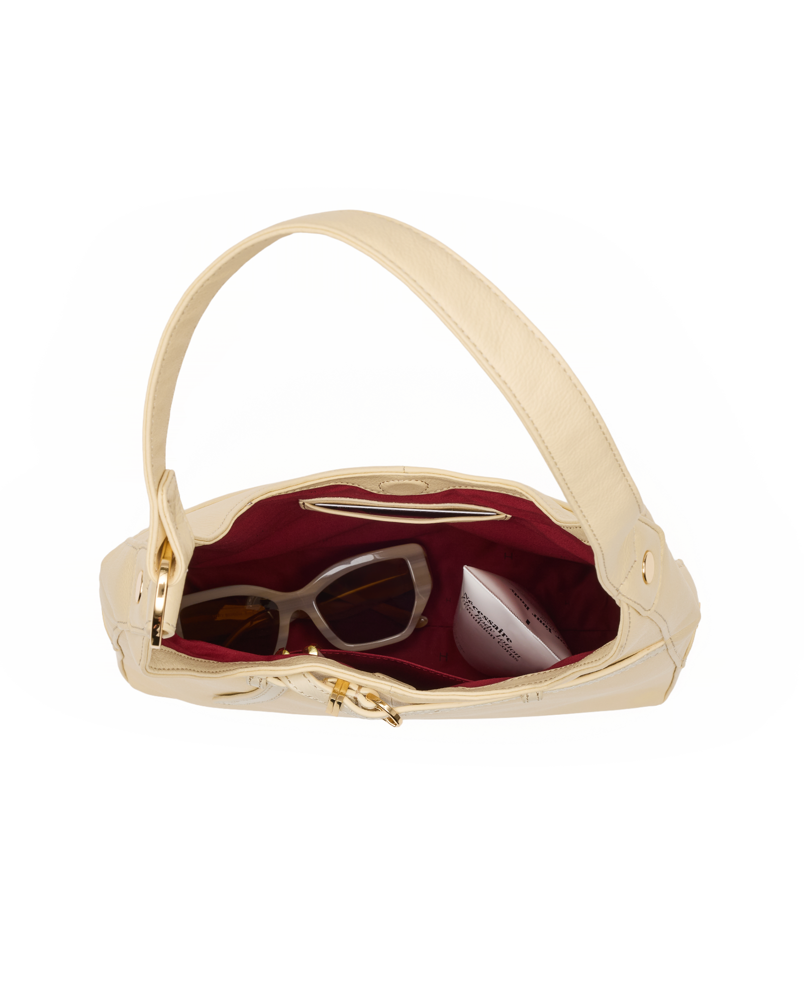 An open cream-colored leather shoulder bag with a burgundy interior, shown against a plain white background. Inside, a pair of sunglasses and a small white cosmetic pouch are visible.