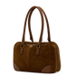 A brown suede handbag with brown leather handles and trim, featuring brass-tone hardware