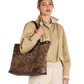A woman models a large brown and gold sequined tote bag with dark brown trim and shoulder straps, worn over her shoulder while wearing a beige shirt and cream shorts against a white background.