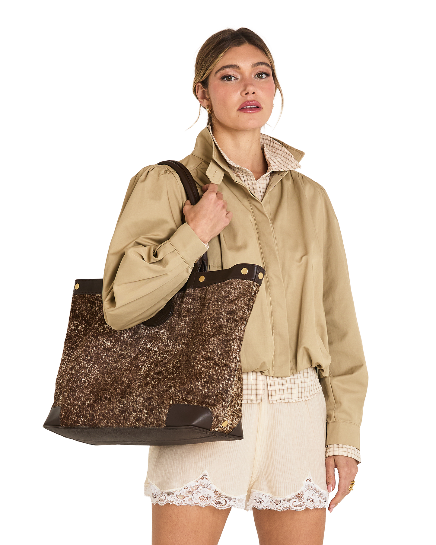 A woman models a large brown and gold sequined tote bag with dark brown trim and shoulder straps, worn over her shoulder while wearing a beige shirt and cream shorts against a white background.