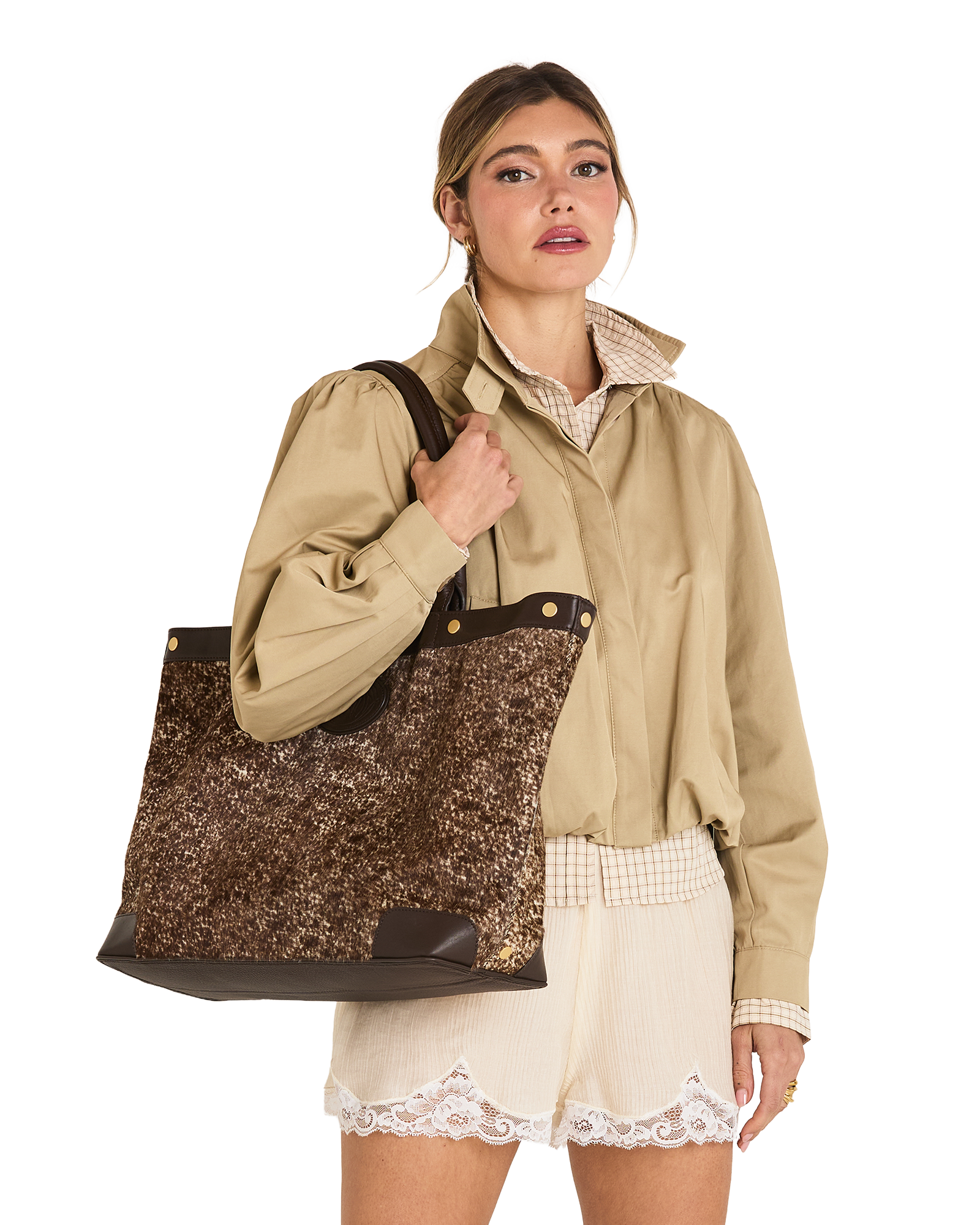 A woman models a large brown and gold sequined tote bag with dark brown trim and shoulder straps, worn over her shoulder while wearing a beige shirt and cream shorts against a white background.