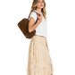 A woman wearing a white t-shirt and a beige ruffled tiered maxi skirt, carrying a brown suede shoulder bag against a plain white background.