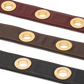 Three leather straps in burgundy, brown, and black, each featuring a row of polished gold-tone circular grommets, displayed diagonally on a white background.