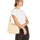 A woman wearing a white t-shirt and dark brown pinstriped trousers carries a light beige leather shoulder bag on her shoulder, shown from a side profile against a solid white background.