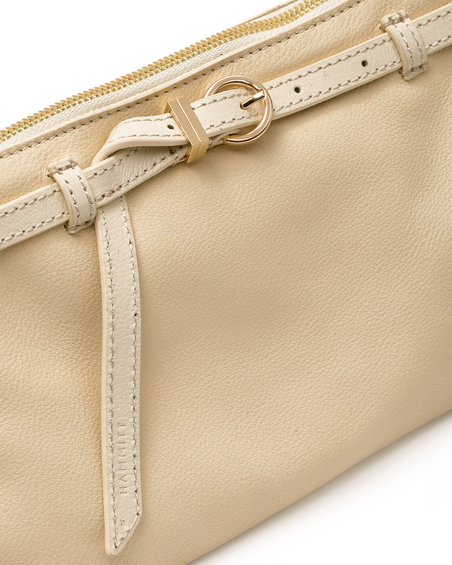 Close-up of a cream-colored leather pouch featuring a matching leather strap with a gold-tone buckle and zipper pull.