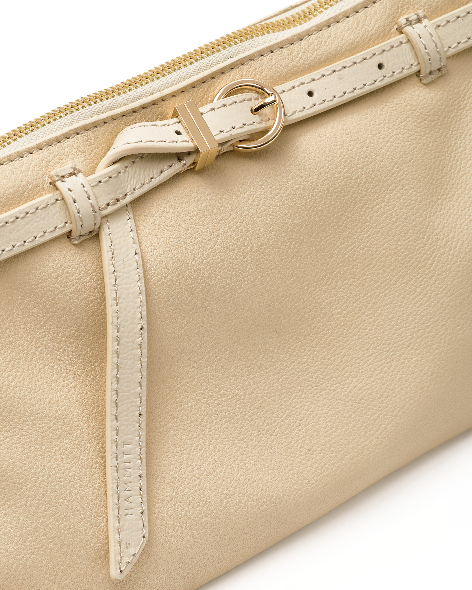Close-up of a cream-colored leather pouch featuring a matching leather strap with a gold-tone buckle and zipper pull.