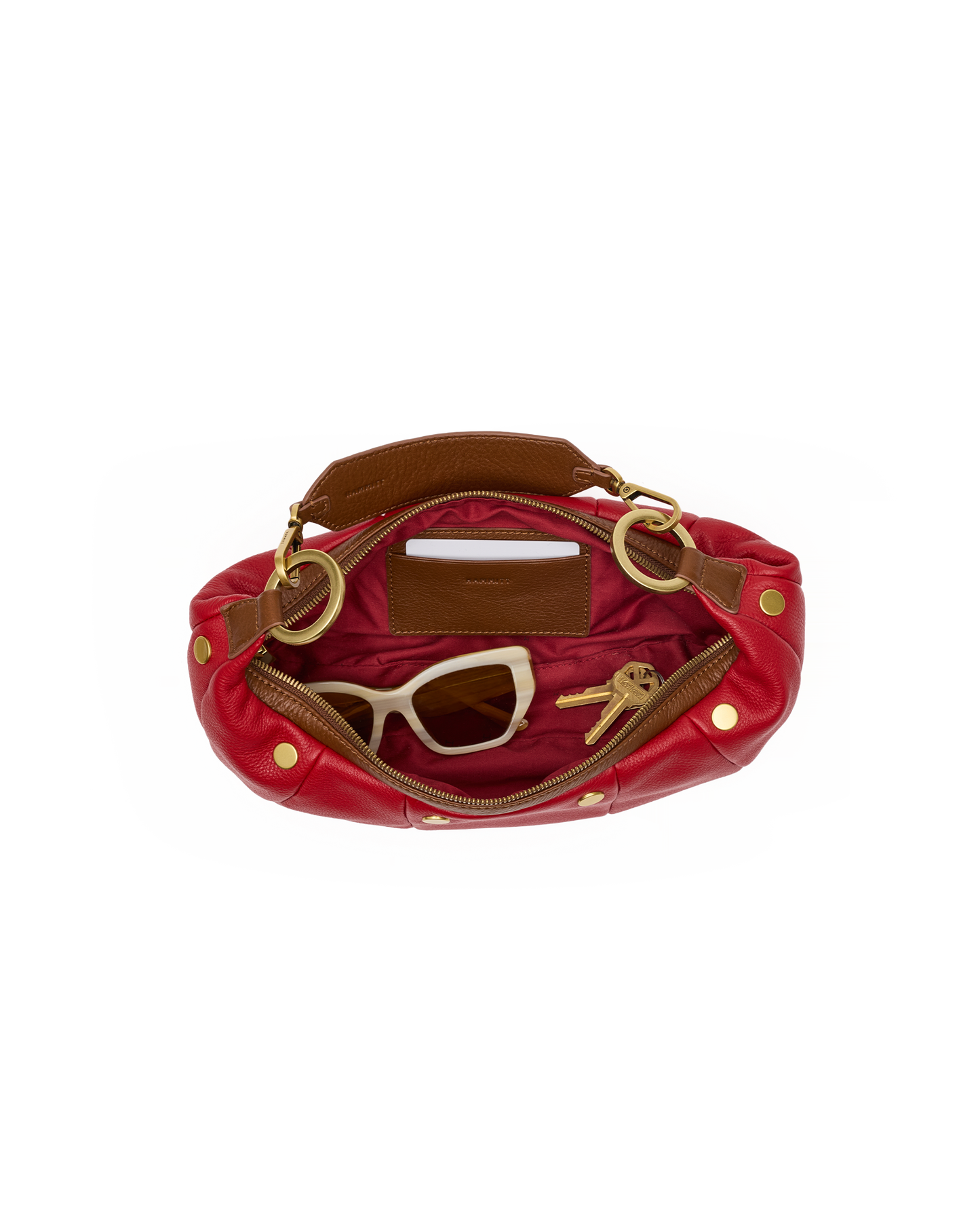 An open red leather shoulder bag with gold-tone hardware, showing a brown interior lining, sunglasses, and keys inside, set against a plain white background.