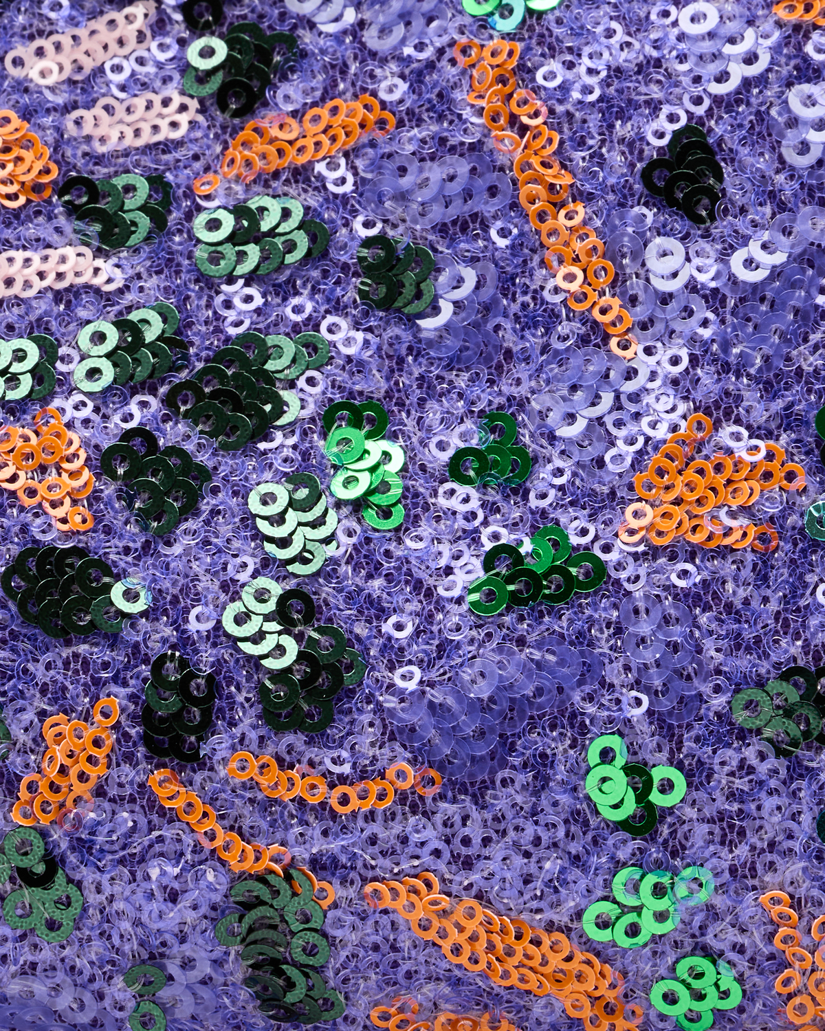 A close-up of a purple sequined fabric featuring scattered accents of green, orange, black, and pale pink sequins.