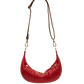 A red crescent-shaped leather shoulder bag with a brown strap and gold-tone hardware, shown against a plain white background.