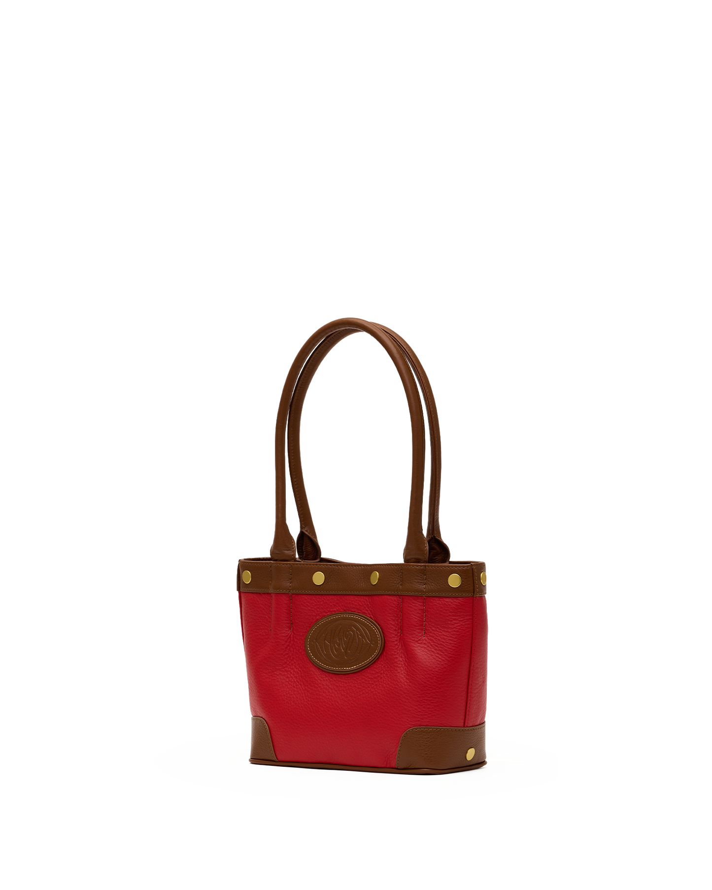 A red leather tote bag with brown leather handles, trim, and corner panels, accented with gold-tone hardware and a circular brown logo patch on the front.