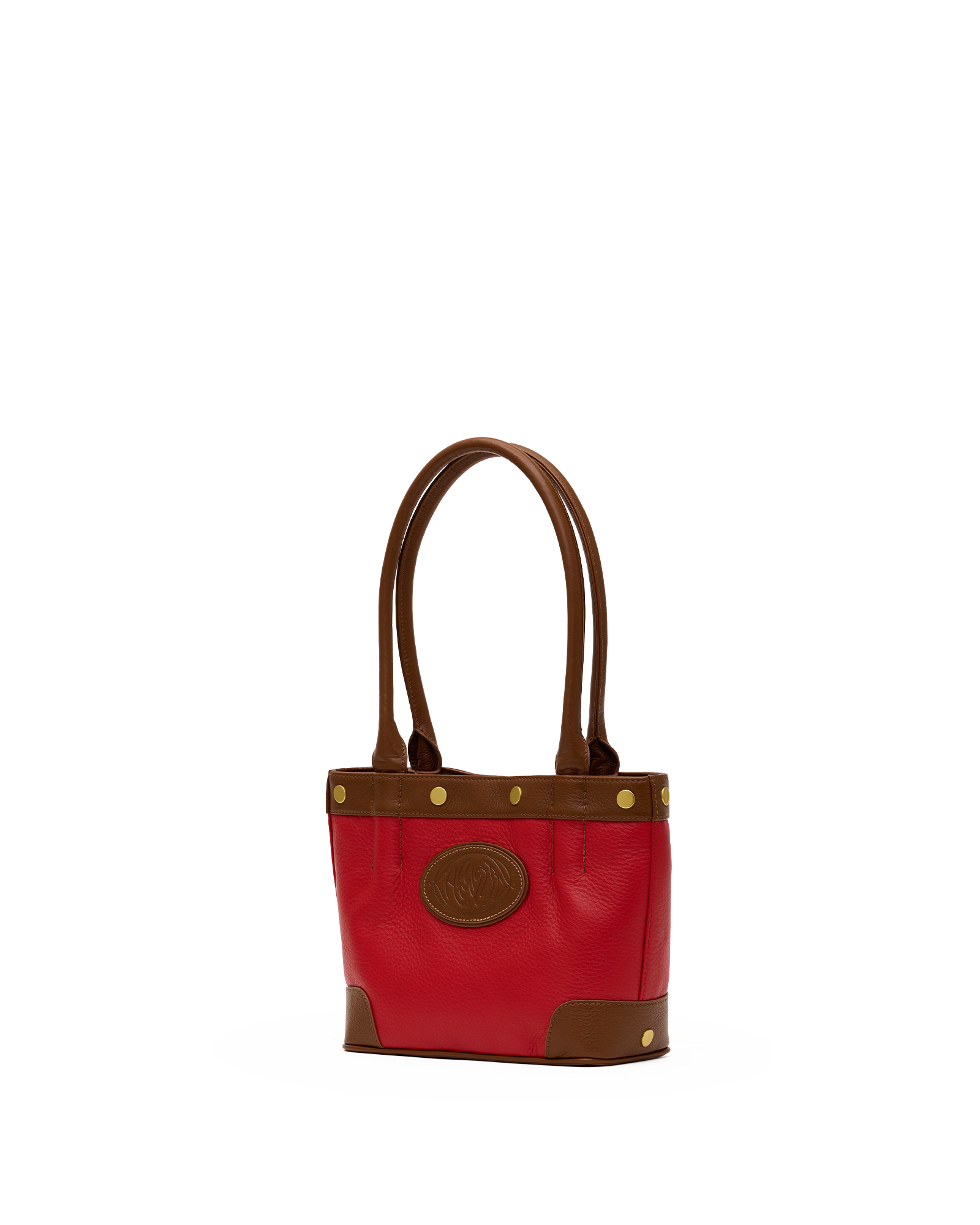 A red leather tote bag with brown leather handles, trim, and corner panels, accented with gold-tone hardware and a circular brown logo patch on the front.