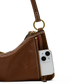 A close-up of a brown textured leather shoulder bag with a gold-tone ring and zipper, shown with a white smartphone inserted into the side zip pocket.