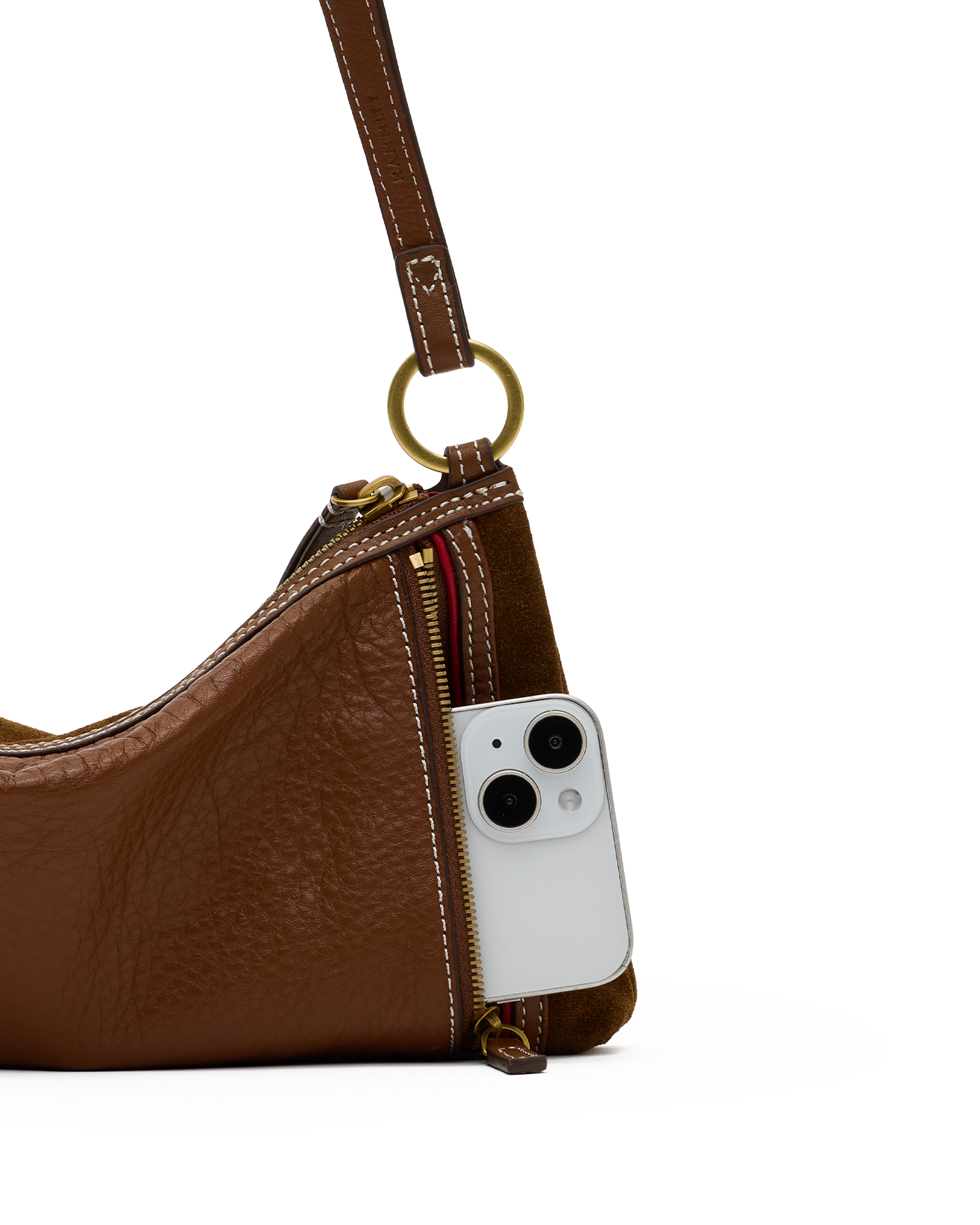 A close-up of a brown textured leather shoulder bag with a gold-tone ring and zipper, shown with a white smartphone inserted into the side zip pocket.