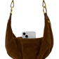 A brown suede crescent shoulder bag with gold-tone hardware and a white smartphone partially tucked into its front slip pocket, shown against a plain white background.