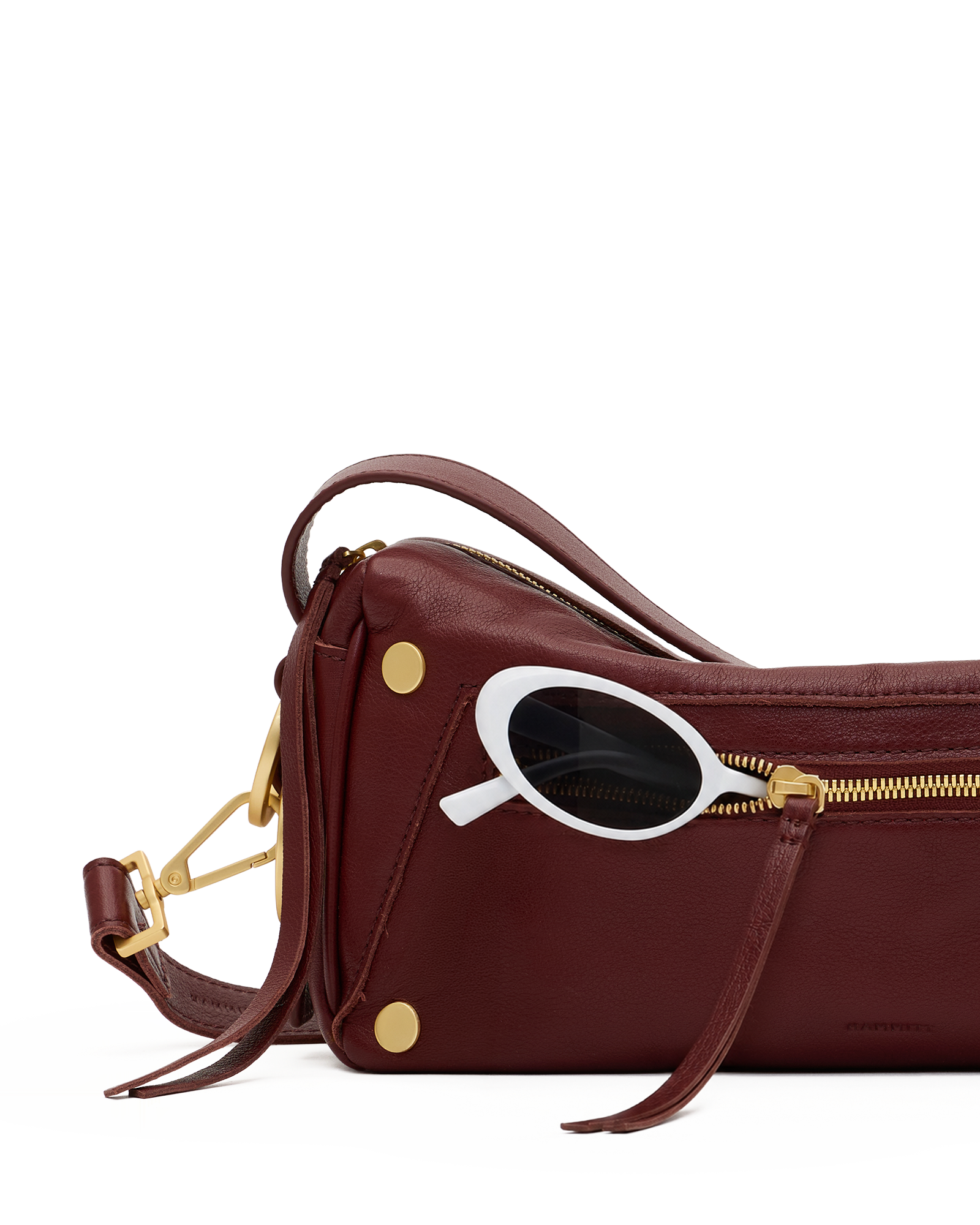 A burgundy leather shoulder bag with gold-tone hardware and a white-framed sunglasses accessory resting on top, shown against a solid white background.