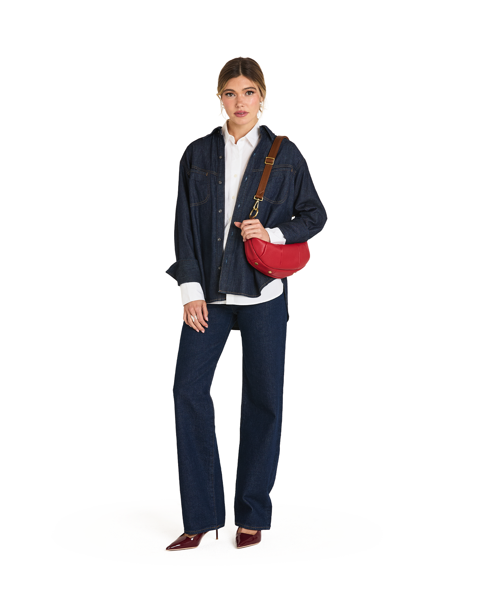 A model stands against a white studio background wearing a dark blue denim jacket and matching wide-leg jeans over a white shirt, with a red crossbody bag and brown heels.