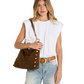 A woman modeling a brown suede shoulder bag with gold-tone studs and a leather strap, styled with a white sleeveless top, light blue jeans, and a tan belt against a plain white background.