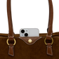 Close-up of a brown suede and leather tote bag with gold-tone hardware, shown against a white background with a silver smartphone partially tucked into the front pocket.