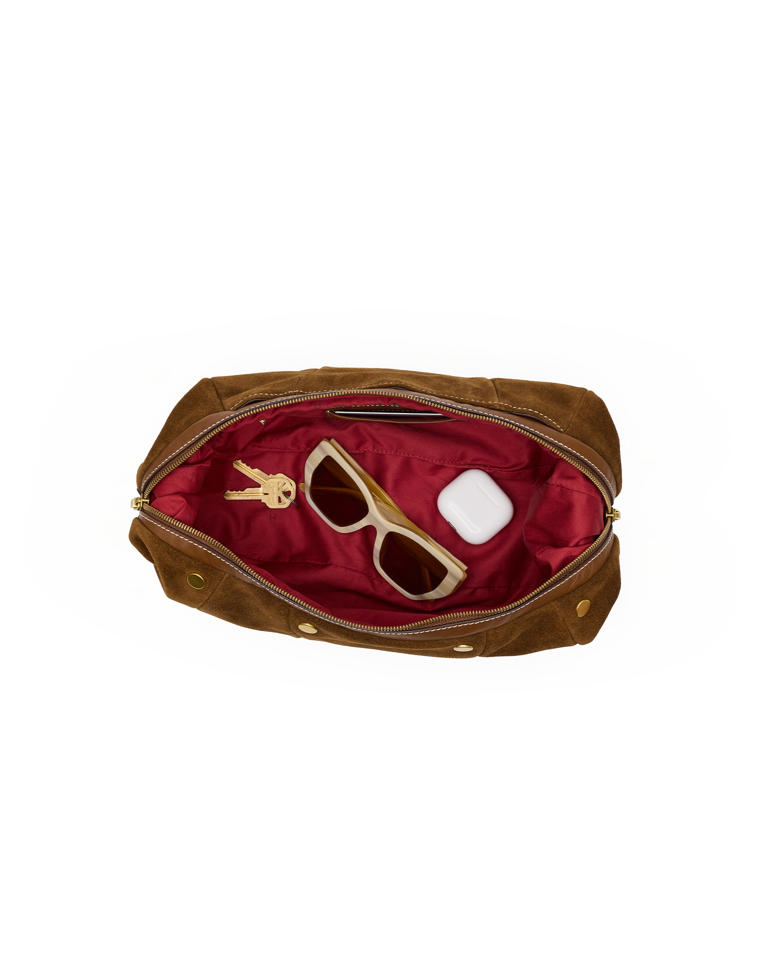 A brown suede cosmetic pouch shown open from above, revealing a deep red satin interior with sunglasses, keys, and a small white item inside. The pouch has gold-tone hardware and is photographed on a plain white background.