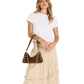 A woman modeling a white short-sleeve t-shirt and a beige tiered maxi skirt, carrying a brown studded shoulder bag with a gold chain strap.