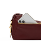 A close-up of a burgundy leather pouch with a gold zipper, showing a silver smartphone partially inserted into the pocket, on a white background.
