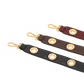 Three leather shoulder straps in black, brown, and burgundy, each featuring gold-tone metal grommets and a swivel snap hook clasp, arranged diagonally on a white background.