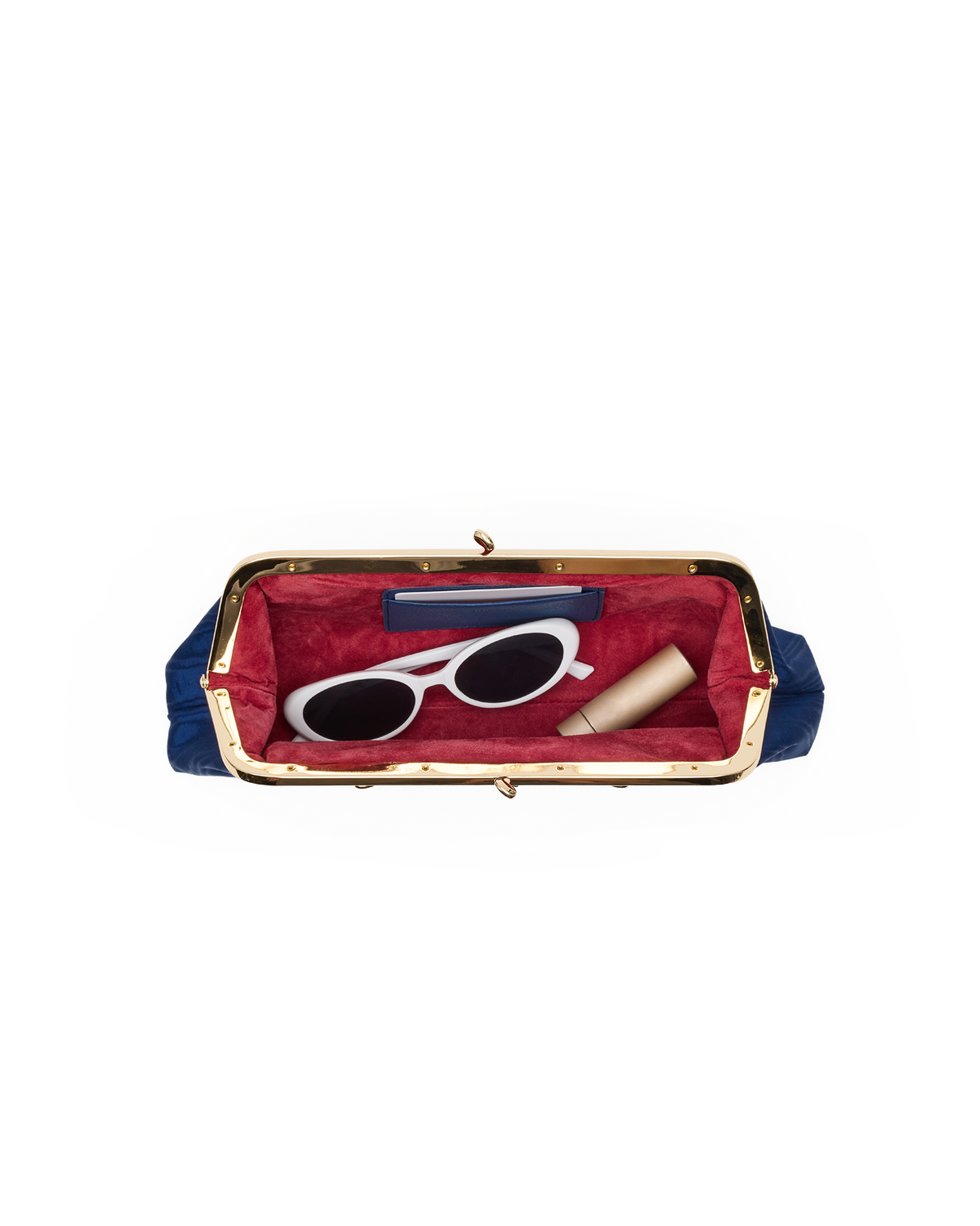 A top-down view of a navy blue and gold kiss-lock clutch bag with a red velvet interior, shown open with white sunglasses, a blue rectangular item, and a beige cylindrical item inside.