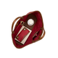 Top-down view of an open tote bag with a deep red interior and brown leather handles, shown filled with a matching red card holder, a brown leather wallet, a white circular item, and a slim pink accessory on a plain white background.