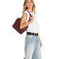 A woman wearing a white sleeveless top, light blue wide-leg jeans, and a black belt with a gold buckle, carrying a dark brown leather tote bag over her shoulder against a plain white background.