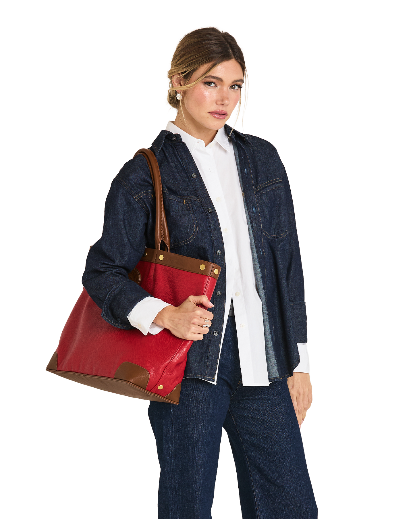 A woman modeling a large red leather tote bag with brown leather trim and gold-tone hardware, styled with a white button-down shirt and a dark denim jacket against a plain white background.
