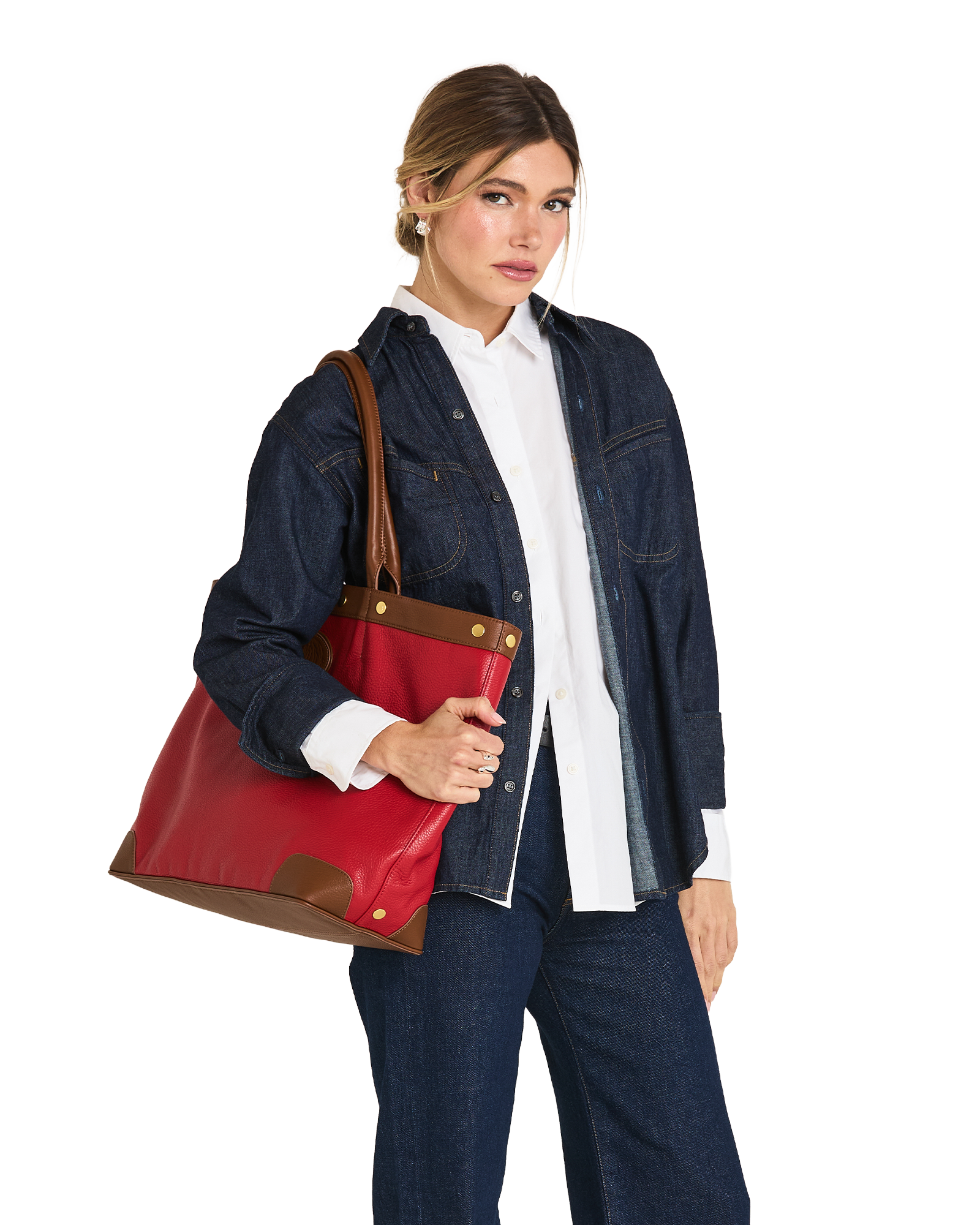 A woman modeling a large red leather tote bag with brown leather trim and gold-tone hardware, styled with a white button-down shirt and a dark denim jacket against a plain white background.