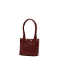 A small leather tote bag in deep burgundy with gold-tone hardware, featuring a circular embossed logo on the front and dual top handles, set against a plain white background.