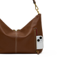 A brown leather shoulder bag with gold-tone hardware, shown on a white background with a white smartphone partially tucked into a side zip pocket.