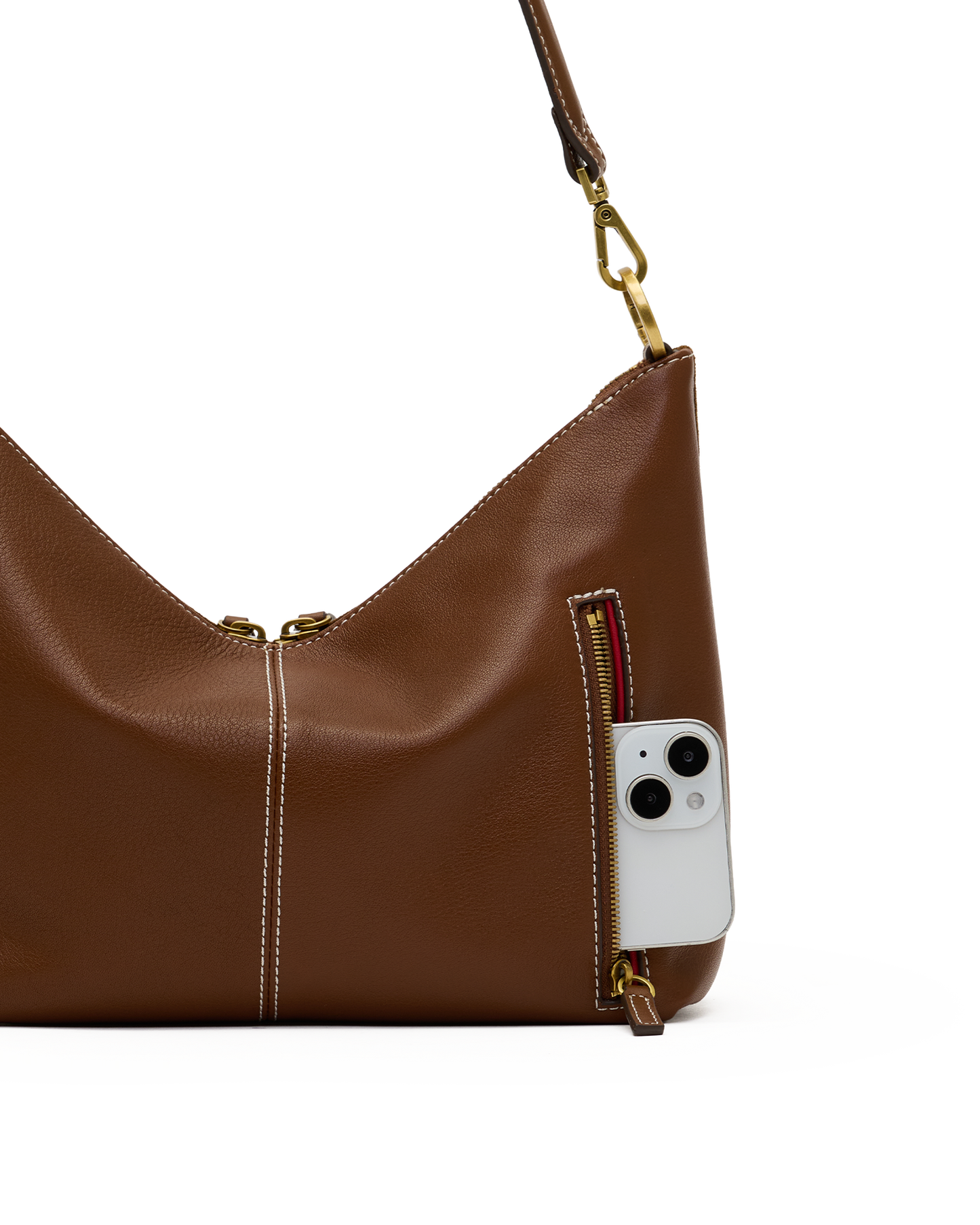A brown leather shoulder bag with gold-tone hardware, shown on a white background with a white smartphone partially tucked into a side zip pocket.