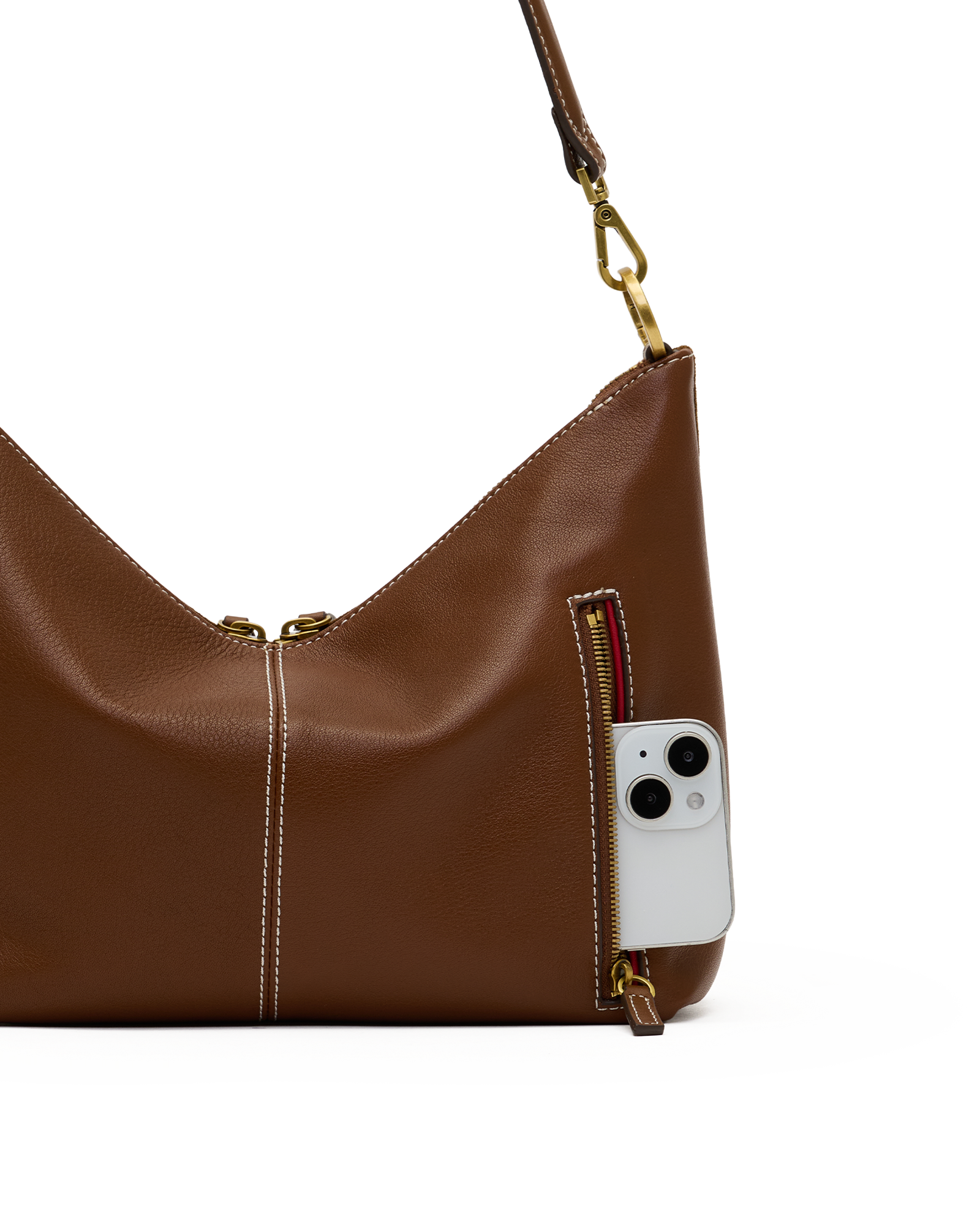 A brown leather shoulder bag with gold-tone hardware, shown on a white background with a white smartphone partially tucked into a side zip pocket.