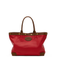 A red leather tote bag with brown leather trim, double top handles, gold-tone hardware, and a circular embossed logo patch on the front, shown against a plain white background.