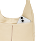 Close-up of a cream-colored pebbled leather shoulder bag with a silver smartphone tucked into its side pocket, set against a solid white background.