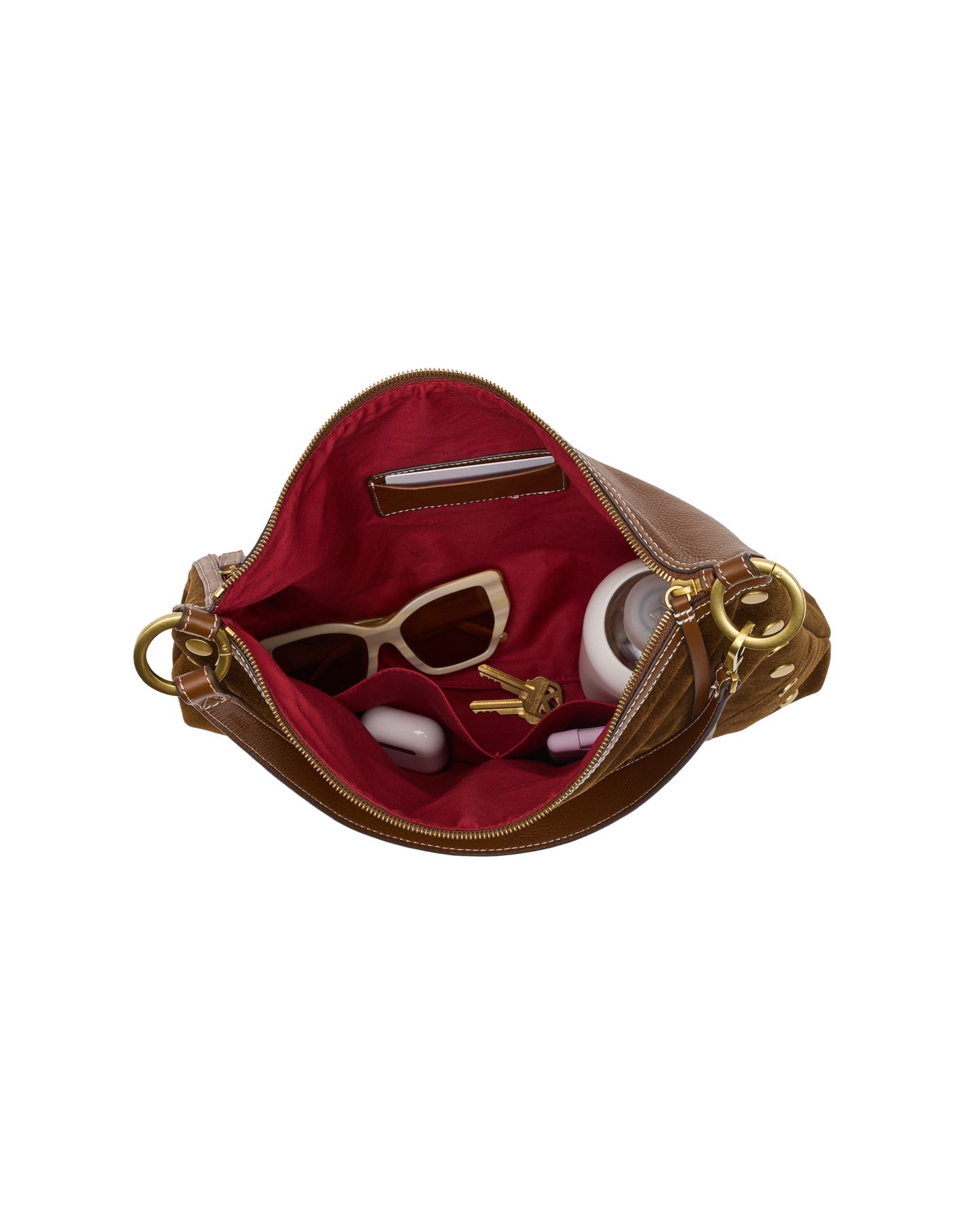 An open brown leather handbag with a bright red interior lining, shown against a plain white background. Inside, the bag is styled with sunglasses, a small wallet, and round white accessories.