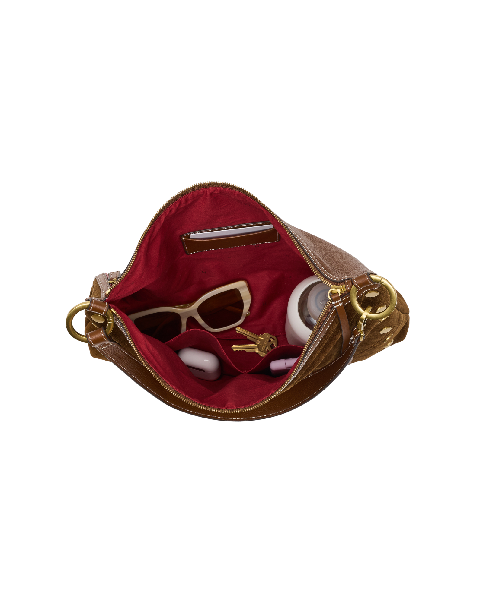 An open brown leather handbag with a bright red interior lining, shown against a plain white background. Inside, the bag is styled with sunglasses, a small wallet, and round white accessories.