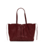 A dark burgundy leather tote bag with double shoulder straps and small gold-tone studs along the bottom edge, displayed on a white circular platform against a solid black background.