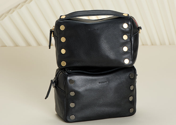 Image of two Evan bags on white backdrop. One Evan crossbody in black burshed gold and second evan crossbody in black gunmetal.