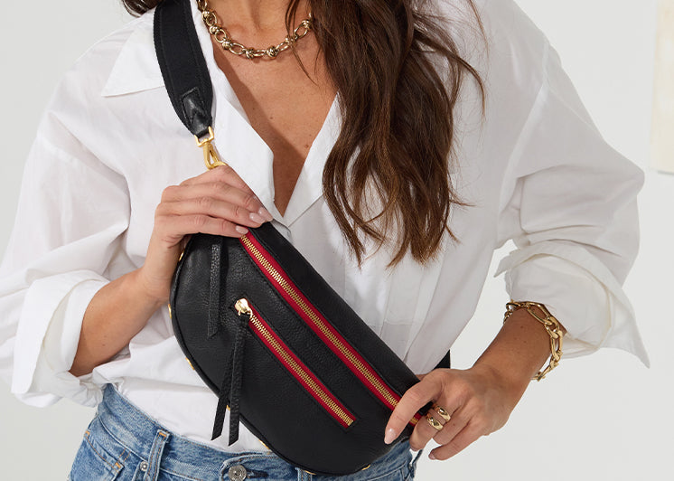 Image of model in white top and blue jeans wearing charles in black brushed gold red zip as crossobody.